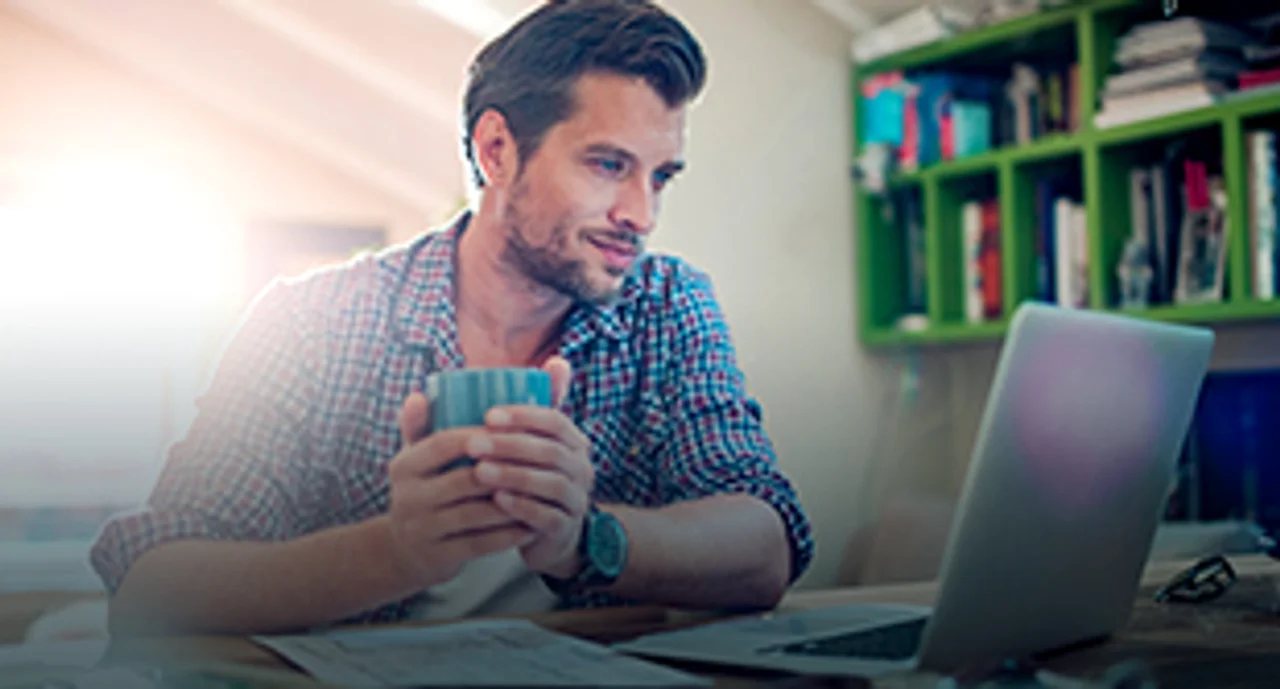 A young man in front of his laptop holding a cup in his hands