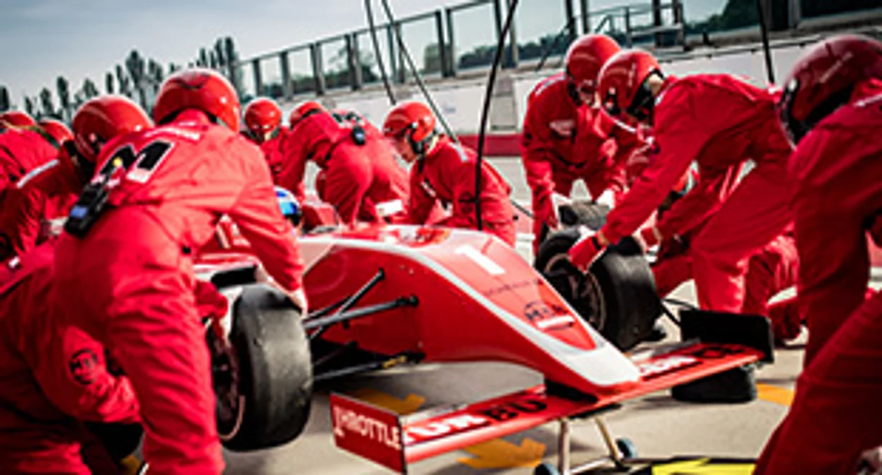 Pit crew in red uniforms changing tires on formula race car during pit stop